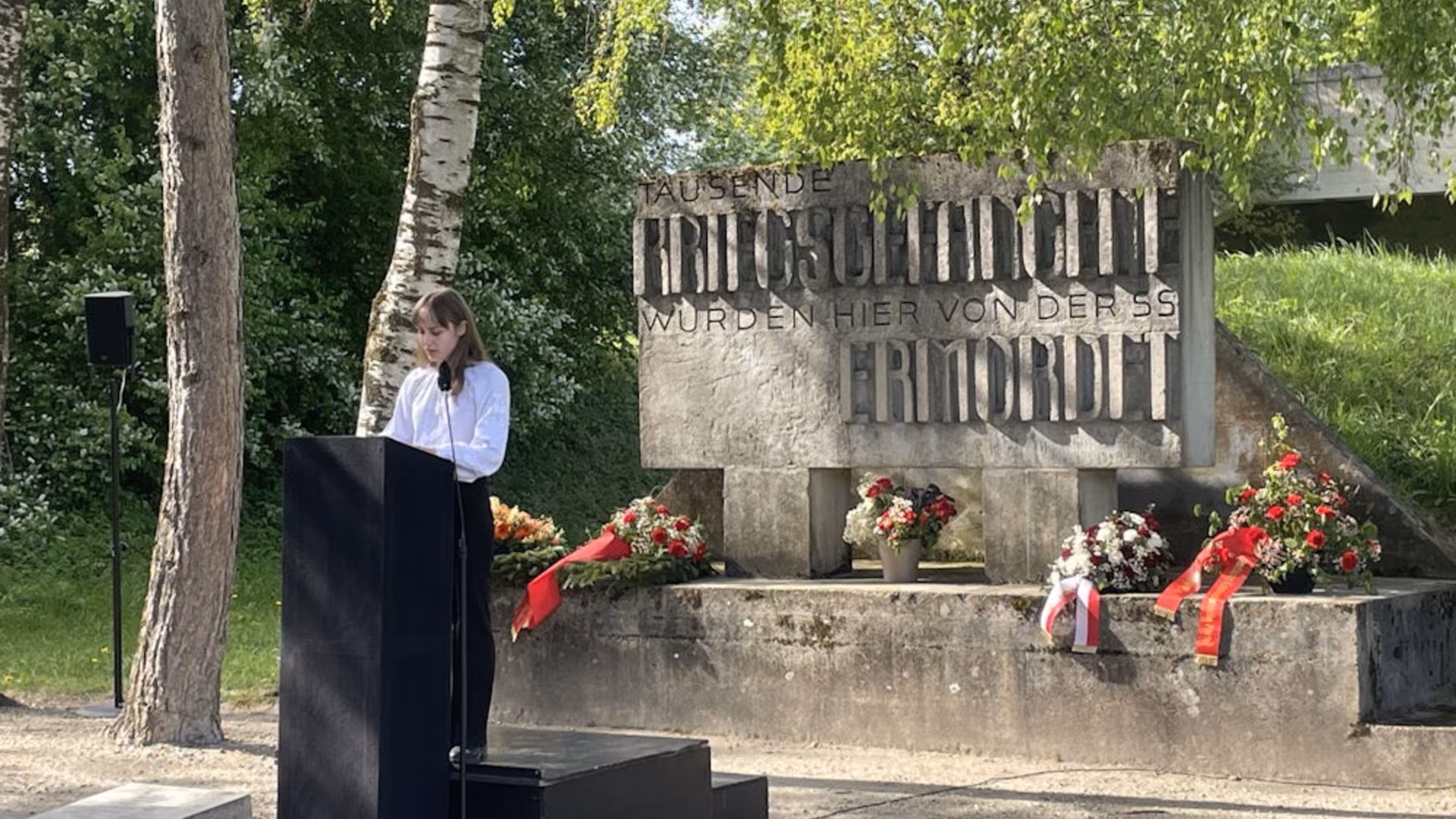 Taler ved podiet foran minnesteinen i Hebertshausen med inskripsjonen «Tausende Kriegsgefangene wurden hier von der SS ermordet», 2. mai 2026